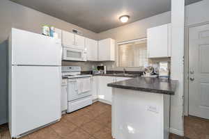 Kitchen with white appliances, tile patterned flooring, a textured ceiling, white cabinets, and sink