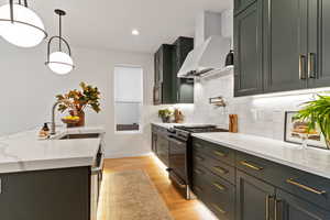 Kitchen featuring pendant lighting, gas stove, wall chimney range hood, light stone counters, and light hardwood / wood-style flooring