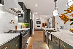 Kitchen with gas stove, decorative light fixtures, premium range hood, sink, and black fridge