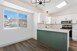 Kitchen with kitchen peninsula, a wealth of natural light, sink, white cabinetry, and appliances with stainless steel finishes