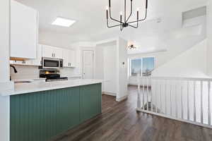 Kitchen featuring white cabinetry, kitchen peninsula, stainless steel appliances, decorative light fixtures, and sink