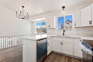 Kitchen with white cabinets, decorative light fixtures, dark hardwood / wood-style flooring, stainless steel appliances, and kitchen peninsula