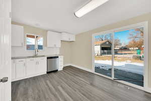 Kitchen with hardwood / wood-style floors, white cabinetry, decorative backsplash, sink, and stainless steel dishwasher