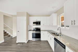 Kitchen with sink, white cabinetry, appliances with stainless steel finishes, dark hardwood / wood-style flooring, and light stone counters