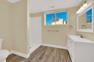 Basement Bathroom featuring wood-type flooring, toilet, vanity, and walk in shower