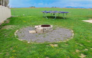 View of yard featuring a fire pit, a trampoline, a rural view, and a fenced backyard