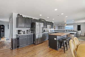 Kitchen with appliances with stainless steel finishes, a kitchen island, butcher block counters, a breakfast bar, and light hardwood / wood-style flooring