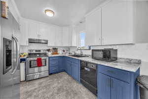 Kitchen with black appliances, white cabinetry, blue cabinetry, backsplash, and sink