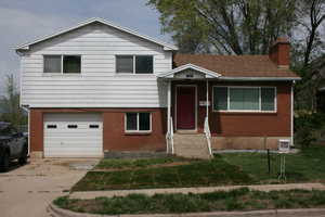 Tri-level home featuring a chimney, concrete driveway, a front lawn, an attached garage, and brick siding