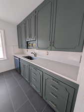 Kitchen with stainless steel dishwasher, green cabinetry, stainless sink, and dark tile patterned floors