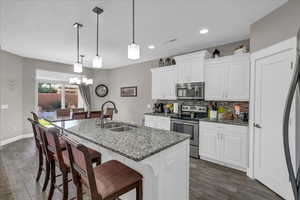 Kitchen with pendant lighting, white cabinets, stainless steel appliances, sink, and a center island with sink