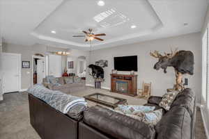 Carpeted living room with ceiling fan with notable chandelier and a tray ceiling