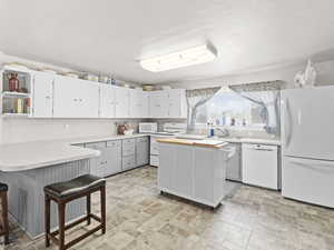 Kitchen featuring white appliances, white cabinets, a kitchen island, sink, and a breakfast bar