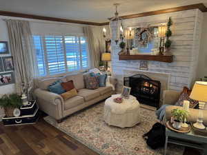 Living room with crown molding, engineered hard wood, a stone fireplace, and a notable chandelier