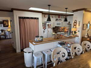 Kitchen featuring kitchen peninsula, butcher block counters, decorative light fixtures, white appliances, and white cabinets