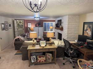 Carpeted home office with a fireplace, a notable chandelier, and a textured ceiling