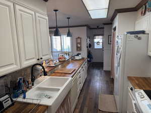 Kitchen with white appliances, butcher block counters, decorative light fixtures, garden sink, and ornamental molding