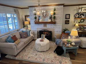 Living room featuring a fireplace, a notable chandelier, ornamental molding, and engineered hard wood