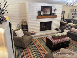 Living room featuring a large fireplace, brick wall, and a chandelier