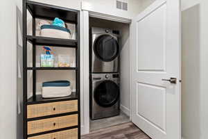 Laundry room with stacked washer and clothes dryer and hardwood / wood-style floors