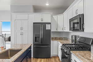 Kitchen with black appliances, white cabinets, sink, and light stone counters