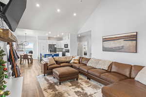 Living room with a notable chandelier, sink, light hardwood / wood-style floors, and high vaulted ceiling