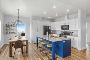 Kitchen with white cabinetry, an island with sink, light stone countertops, black appliances, and sink