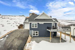 Snow covered back of property with a deck and a garage