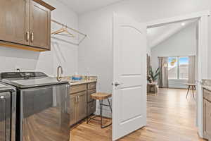 Laundry room with light wood-type flooring, cabinets, washer and clothes dryer, and sink