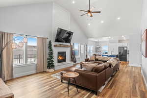 Living room featuring ceiling fan, a large fireplace, light hardwood / wood-style flooring, and high vaulted ceiling