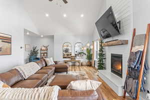 Living room featuring light hardwood / wood-style floors, high vaulted ceiling, ceiling fan, and a fireplace