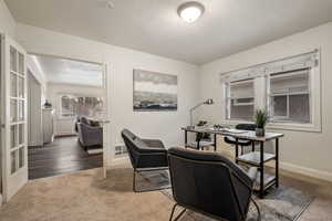 Office area with a textured ceiling, dark colored carpet, and french doors