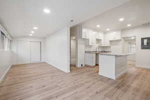 Kitchen with white cabinets, light wood-type flooring, light stone counters, and a center island