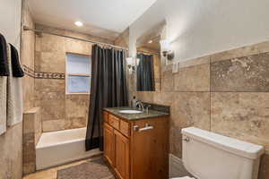 Full bathroom with toilet, tile walls, shower / bath combination with curtain, and vanity