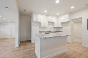 Kitchen featuring white cabinetry, light hardwood / wood-style floors, light stone counters, and a kitchen island