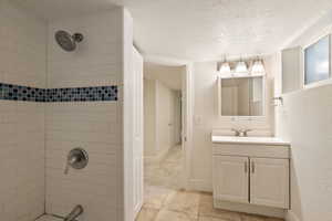 Bathroom featuring a textured ceiling, a tile shower, and vanity