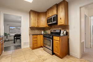 Kitchen featuring decorative backsplash, appliances with stainless steel finishes, dark stone countertops, and light tile patterned flooring