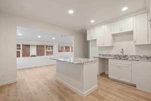 Kitchen with light stone countertops, white cabinets, and sink