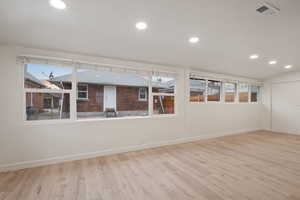 Spare room featuring light wood-type flooring and vaulted ceiling