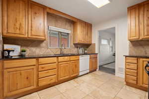 Kitchen featuring sink, dark stone countertops, dishwasher, and light tile patterned flooring