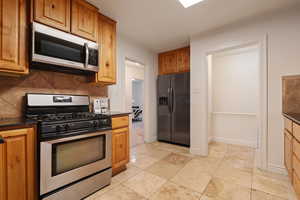 Kitchen featuring light tile patterned floors, backsplash, appliances with stainless steel finishes, and dark stone counters