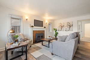 Living room featuring a brick fireplace, hardwood / wood-style floors, crown molding, and a textured ceiling