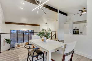 Dining area featuring lofted ceiling with beams, light wood-type flooring, and ceiling fan with notable chandelier