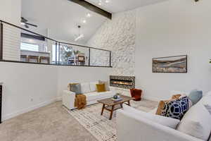 Living room featuring light carpet, ceiling fan, a fireplace, and lofted ceiling with beams