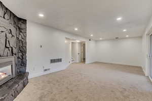 Unfurnished living room featuring light carpet and a stone fireplace