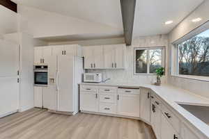 Kitchen with white cabinetry, light hardwood / wood-style flooring, lofted ceiling with beams, and white appliances