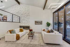 Carpeted living room featuring a tiled fireplace, vaulted ceiling with beams, and a notable chandelier