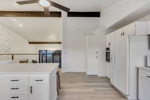 Kitchen featuring white cabinetry, stainless steel oven, white fridge with ice dispenser, and beamed ceiling