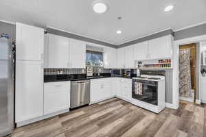 Kitchen with appliances with stainless steel finishes, backsplash, white cabinets, light hardwood / wood-style flooring, and sink