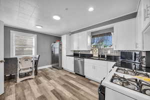 Kitchen featuring white cabinets, stainless steel appliances, tasteful backsplash, sink, and light hardwood / wood-style flooring